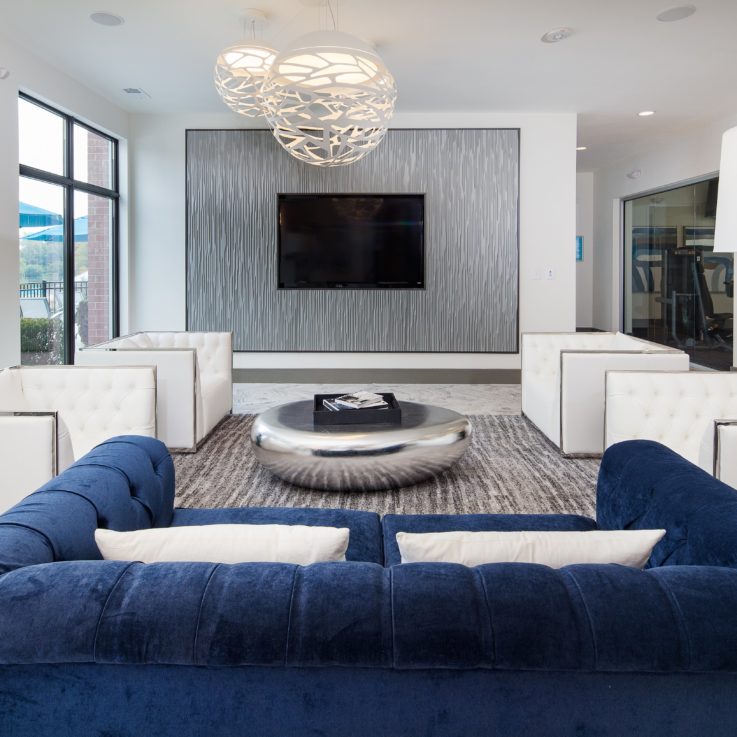 Seating area with a blue couch, white chairs, and a flatscreen television