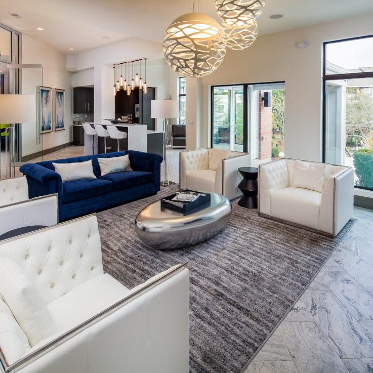 Seating area with a blue couch, white chairs, and a stainless steel coffee table