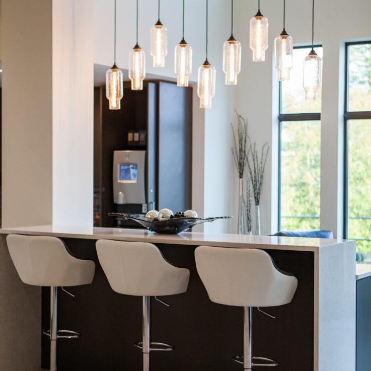 Three white barstools next to a white counter and hanging lights
