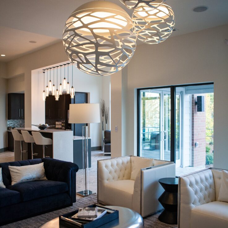 Two white chairs, a blue couch, a stainless steel coffee table, and three hanging lights