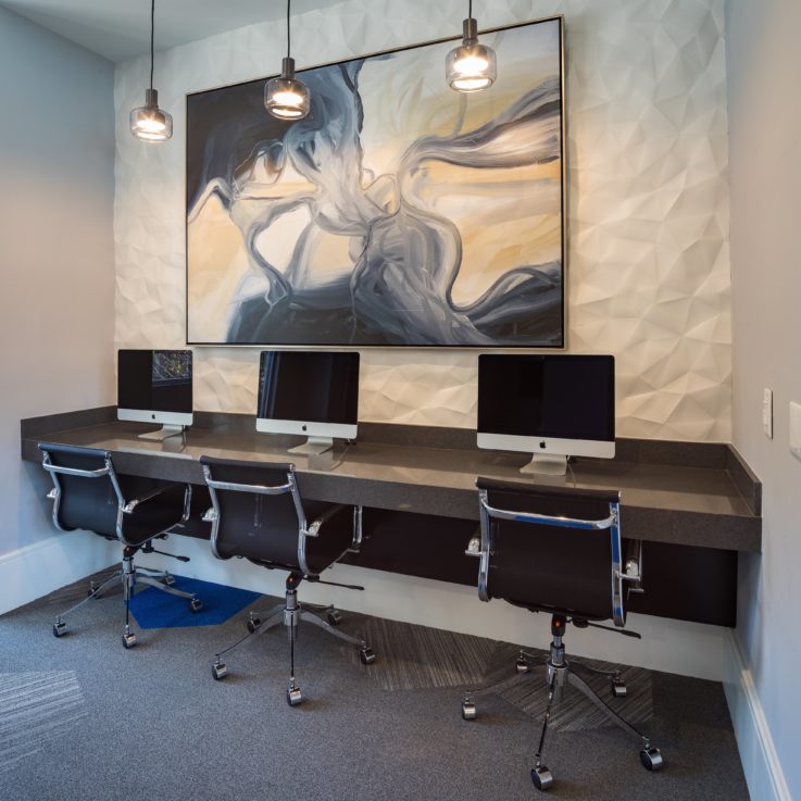 Shared desk with three computers and an abstract painting