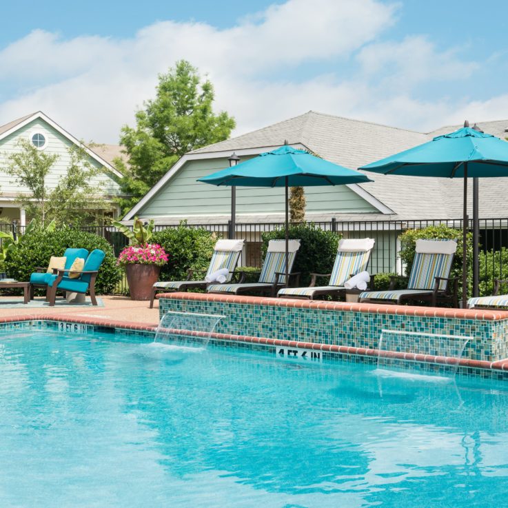 Pool with a fountain and beach chairs under teal umbrellas