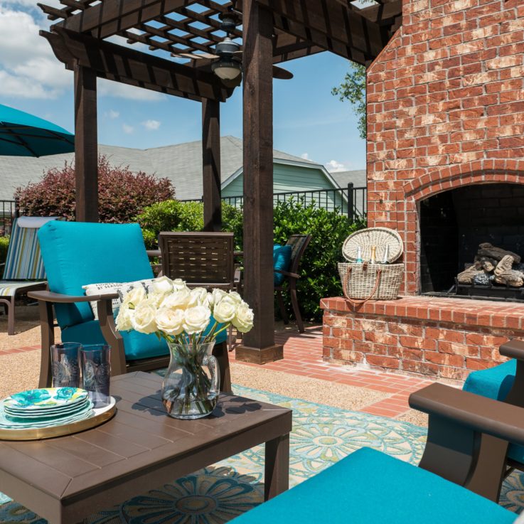Outdoor seating area with dark wooden chairs, teal cushions, and a brick fireplace