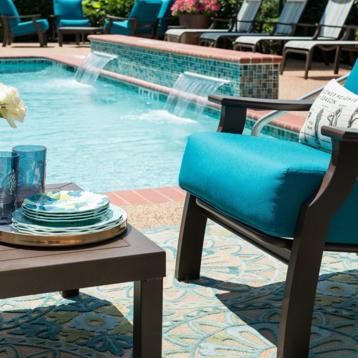 Closeup of a chair and table with plates and the outdoor pool in the background