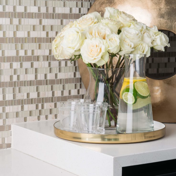 Serving tray four glasses, a jug of water, and white roses on a white counter