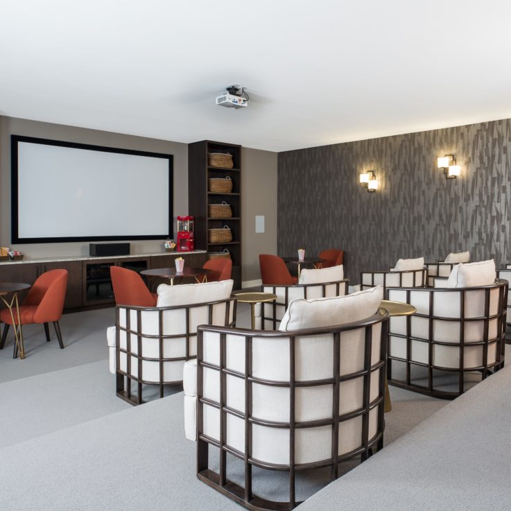 Eight wooden chairs with white cushions in front of a projector screen