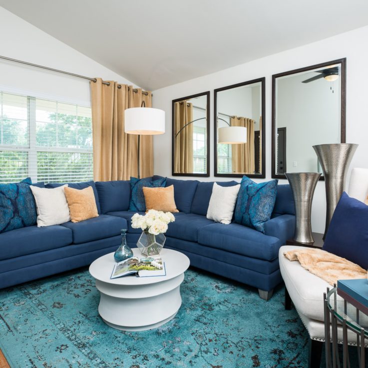 A blue couch, white chair, and white coffee table with three mirrors on the wall