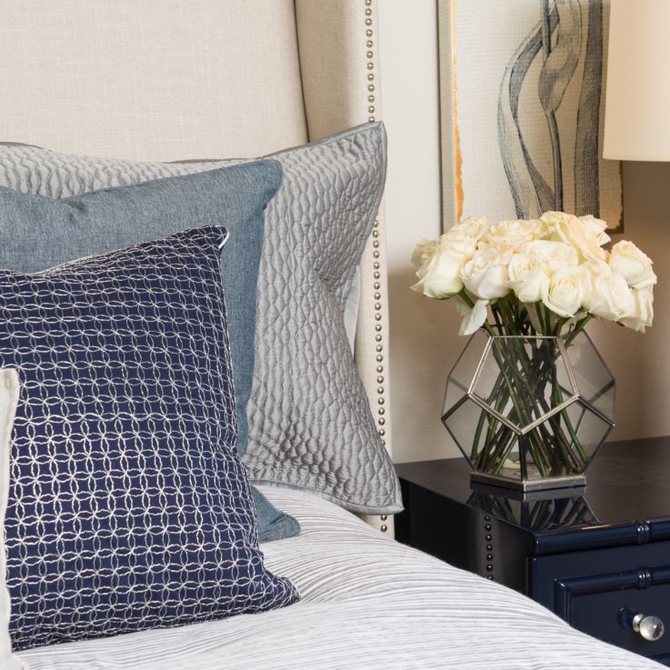 Closeup of pillows on a bed next to a bedside table with white roses