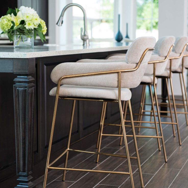 Five brass barstools with white cushions sitting at a white countertop