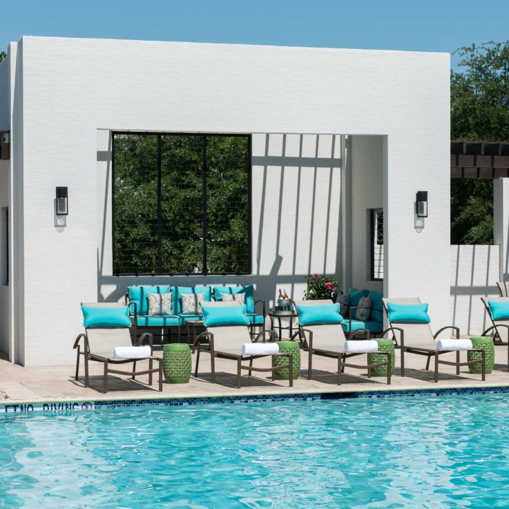 Beach chairs with teal pillows next to an outdoor pool