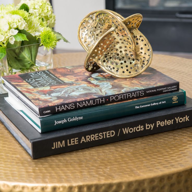 Three books on a coffee table next to flowers in a glass container
