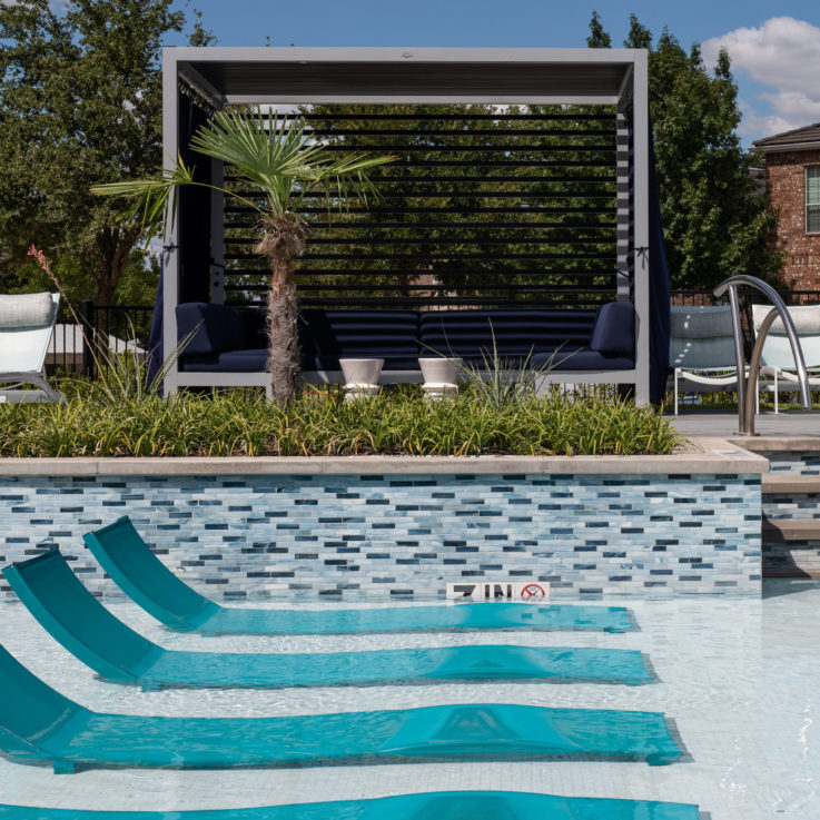 Teal chairs in the shallow end of a pool with a cabana in the background