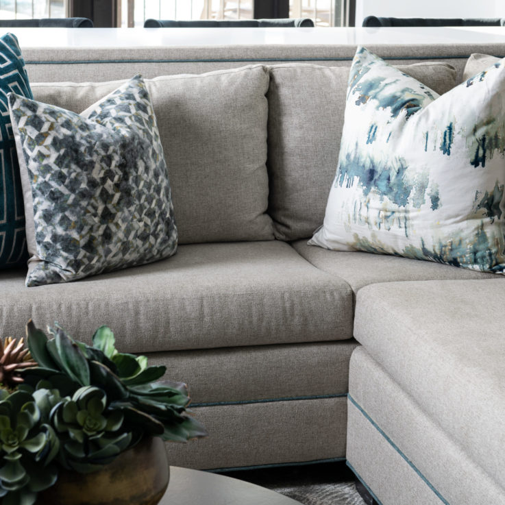 Light gray corner couch with three blue, gray, and white pillows