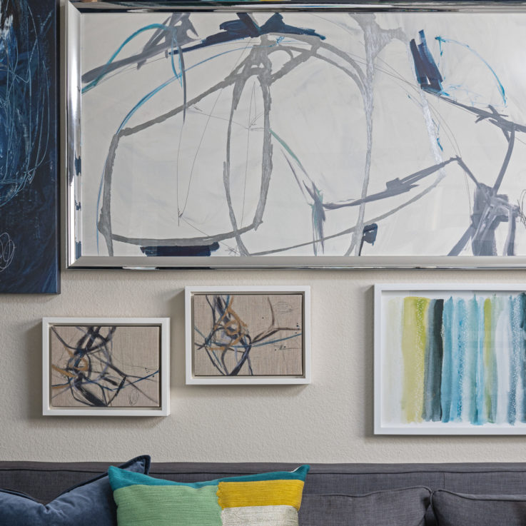Various abstract paintings hanging above a gray couch
