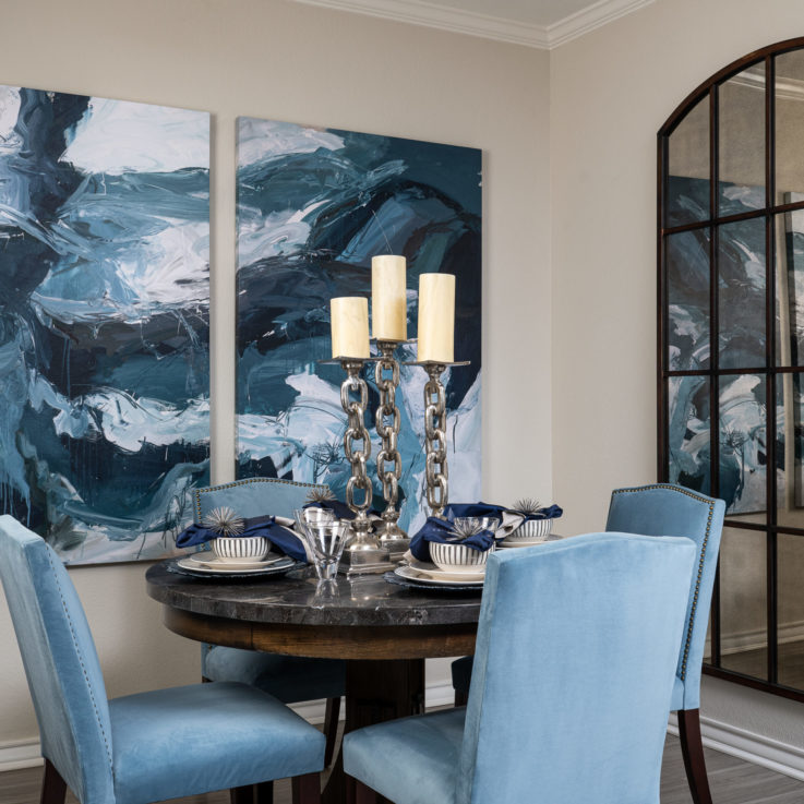 Dining area with a dark marble table, four blue chairs, and two blue, abstract paintings hanging on the wall