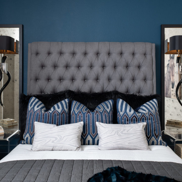 Queen bed with blue pillows and two clear nightstands against a blue wall