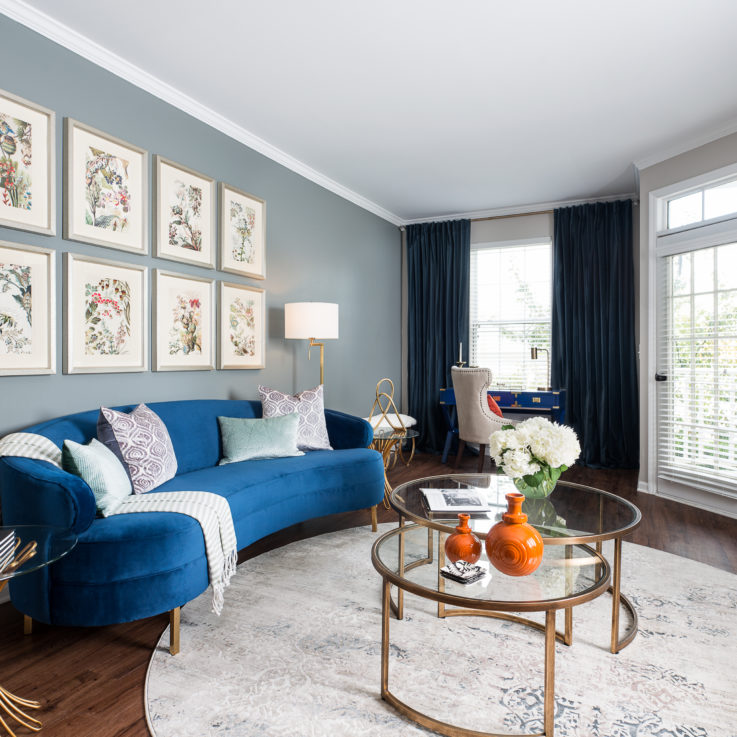 Blue curved couch, a glass coffee table, and a white rug