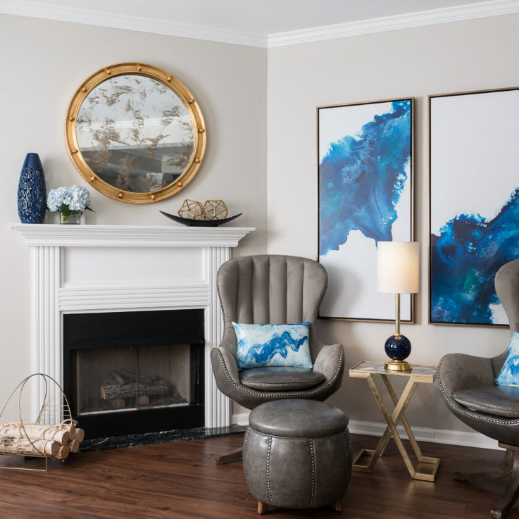 Two gray leather chairs next to a fireplace and two abstract paintings