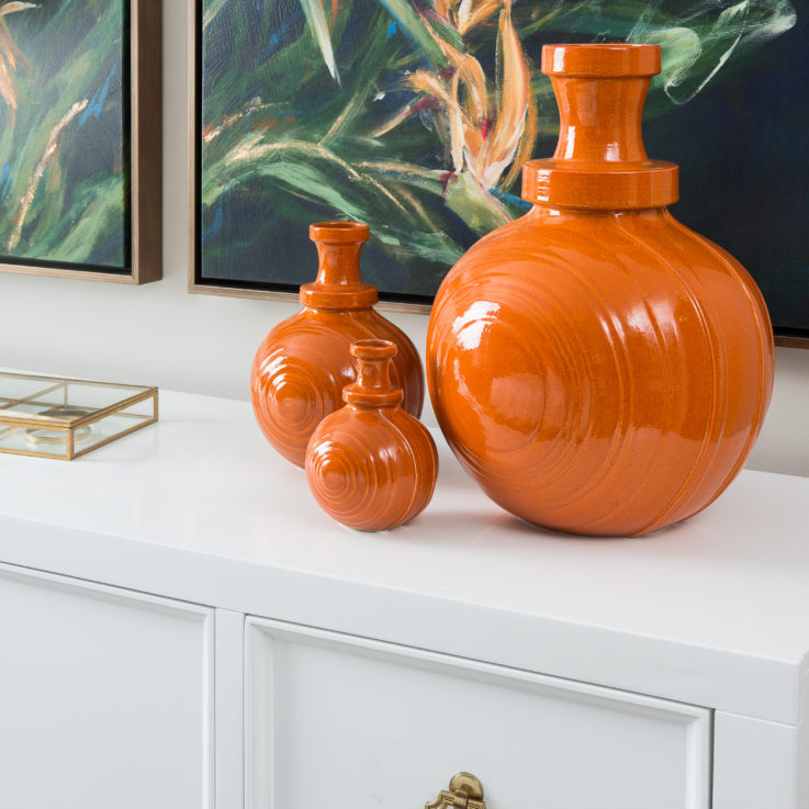 Three orange jugs on a white cabinet