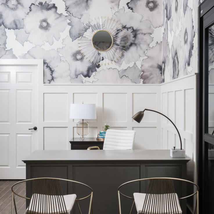 Dark brown desk with two brass chairs and white paneled wall