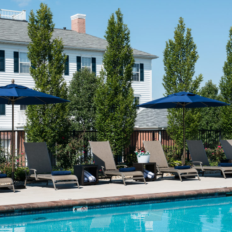 Beach chairs by an outdoor pool with dark blue umbrellas
