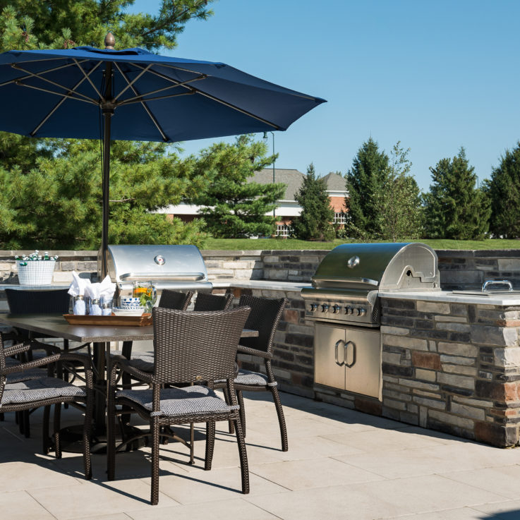 Outdoor grill area with a brown table with eight brown chairs and a dark blue umbrella