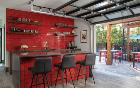 Bar area with dark gray countertops, black chairs, and red tiled walls