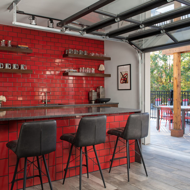 Bar area with dark gray countertops, black chairs, and red tiled walls
