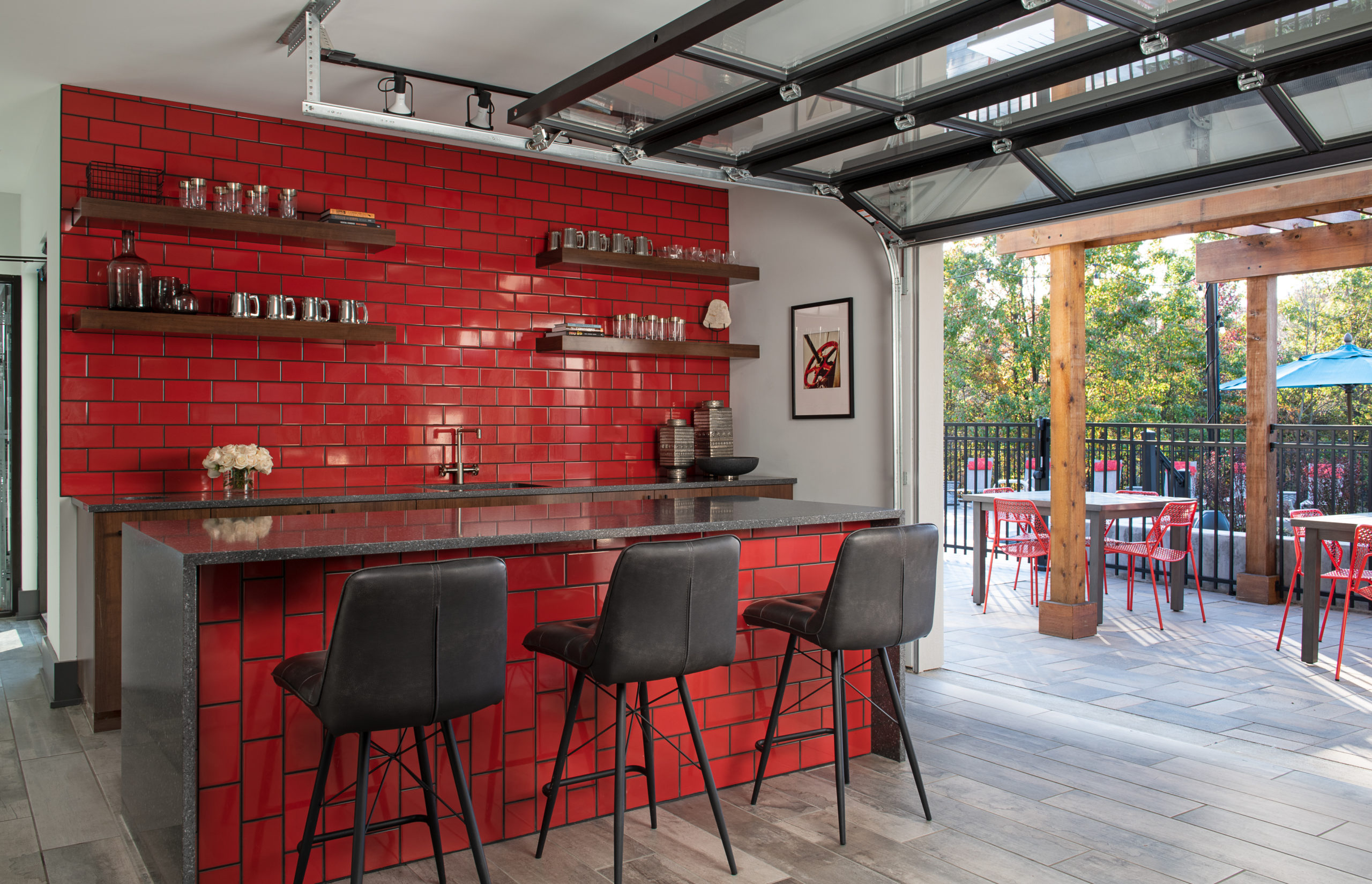 Bar area with dark gray countertops, black chairs, and red tiled walls