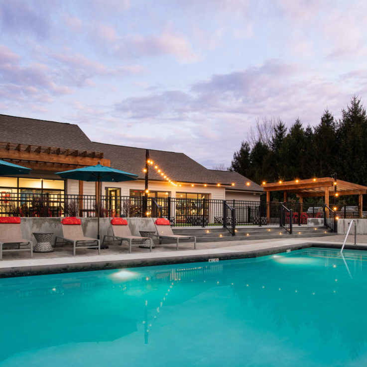 Outdoor pool at dusk with beige beach chairs and teal umbrellas