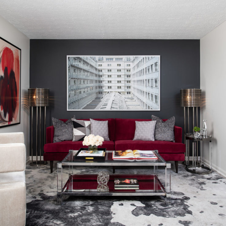 Purple couch with gray pillows and a glass coffee table beneath a painting