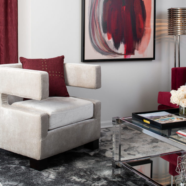 White chair with a red pillow in front of red curtains