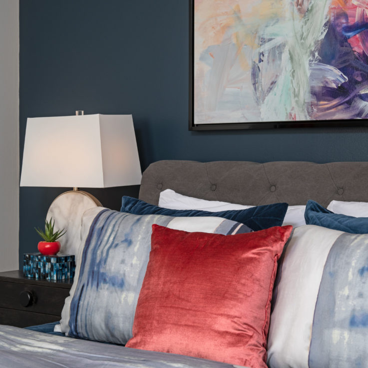 Bed with white, blue, and red pillows next to a dark gray nightstand