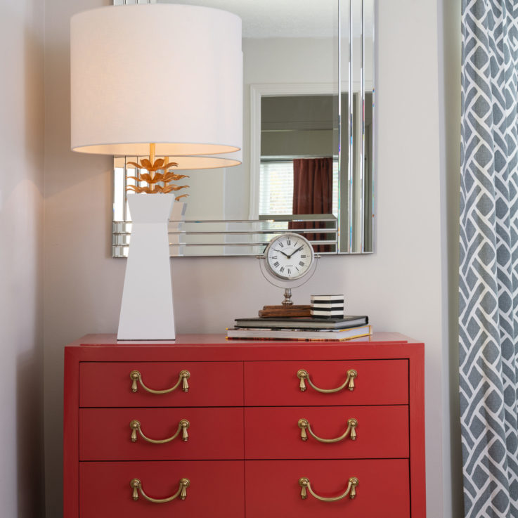 Red dresser with a white lamp and a framed mirror