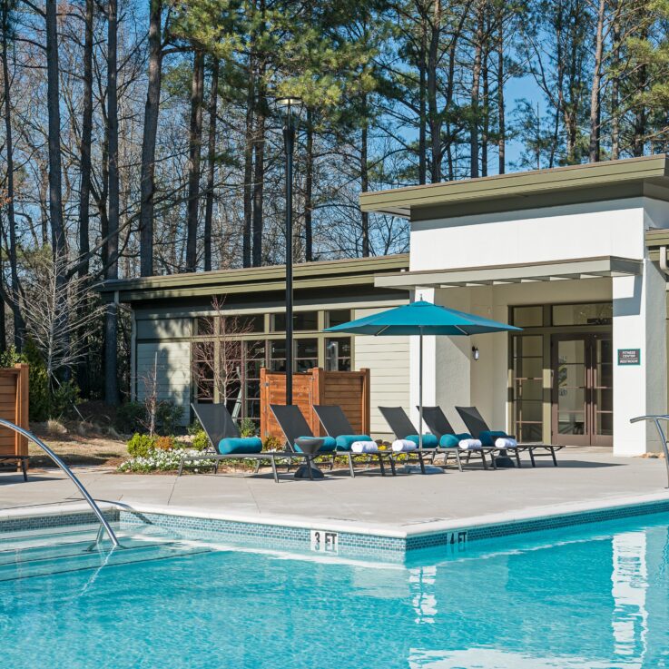 Outdoor pool with beach chairs with teal pillows and umbrellas