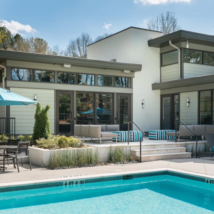 Outdoor pool with seating, tables, and umbrellas in front of a clubhouse