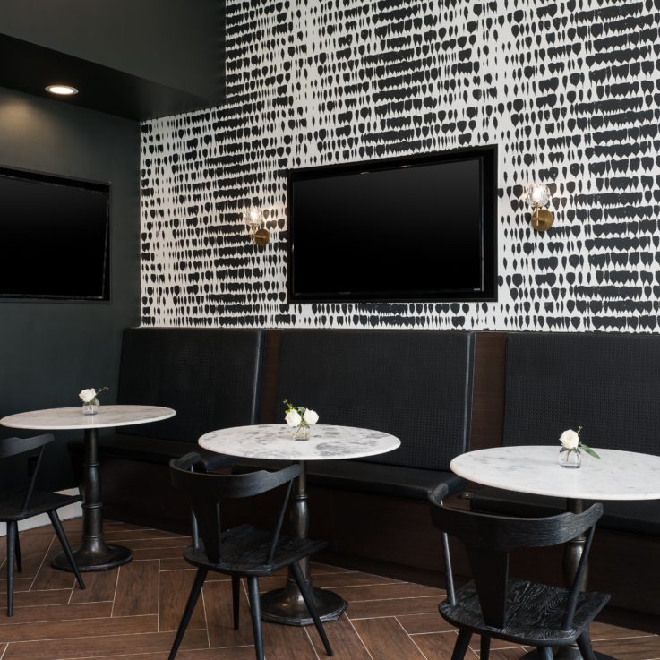 White tables with black booths and chairs beneath flatscreen televisions
