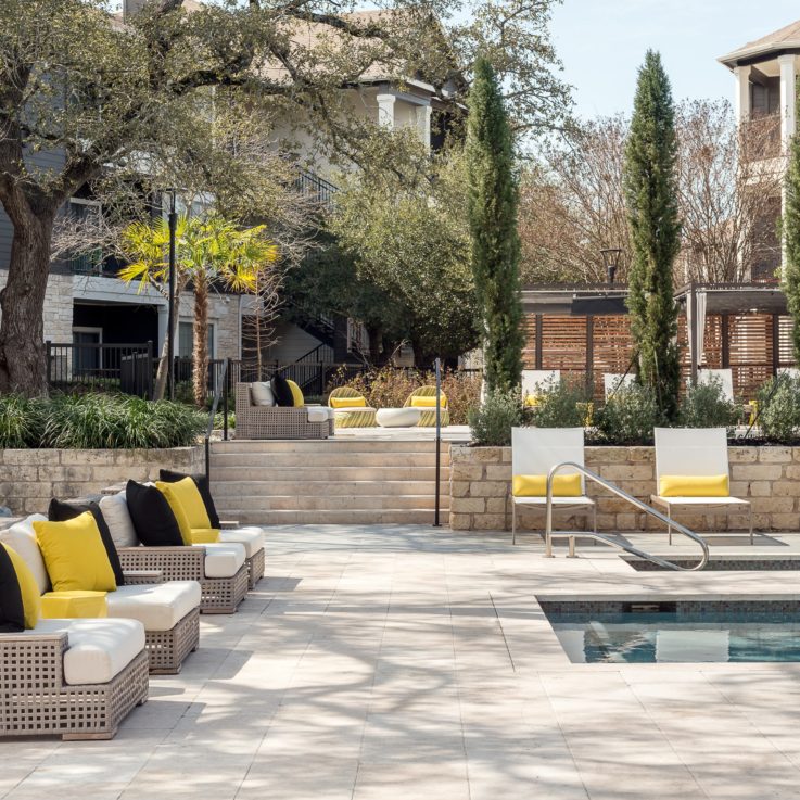 Wicker seats and beach chairs with black and yellow pillows next to an outdoor pool