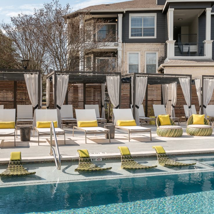 Beach chairs with yellow pillows and cabanas next to an outdoor pool