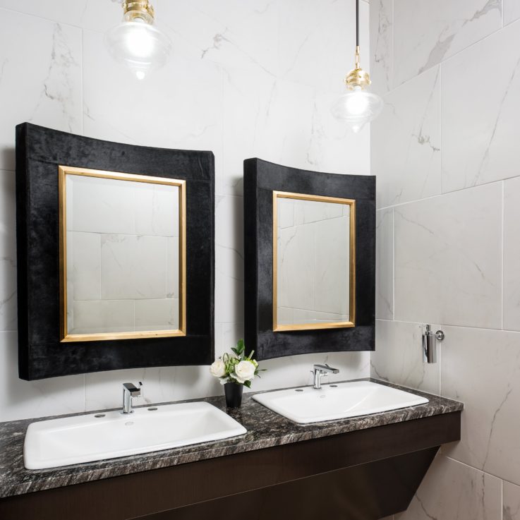 Two white sinks on a marble countertop with two mirrors
