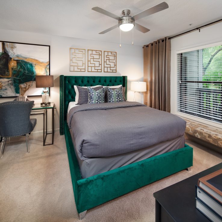 Green twin bed with dark gray sheets next to a glass desk