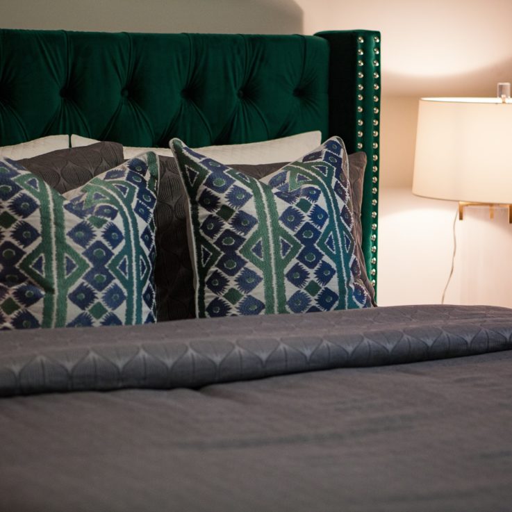 Bed with a green headboard, dark gray sheets, and a lamp on a nightstand