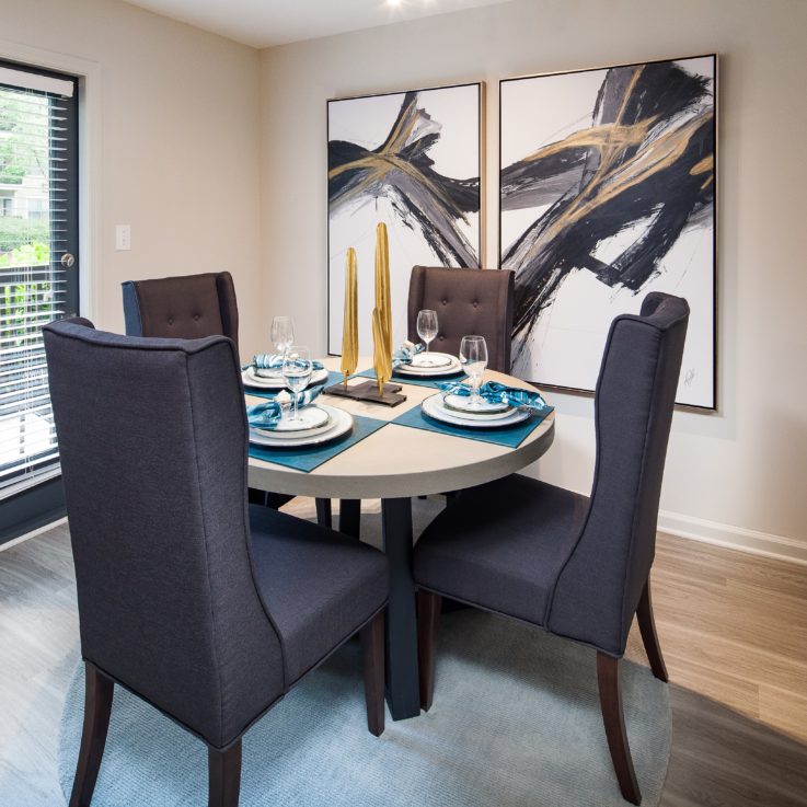 Circular dining table with four dark gray chairs and two abstract paintings