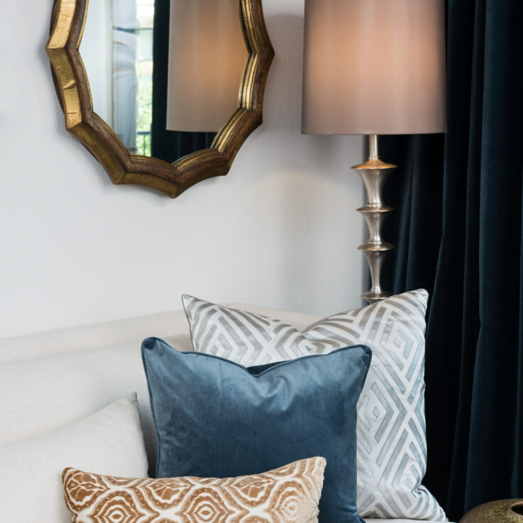 White couch with three cushions, a standing lamp, and a wall mirror