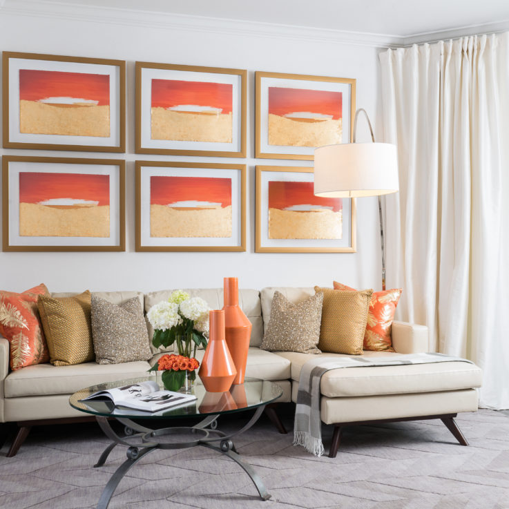 Beige couch with orange, gold, and brown pillows and six identical paintings on the wall