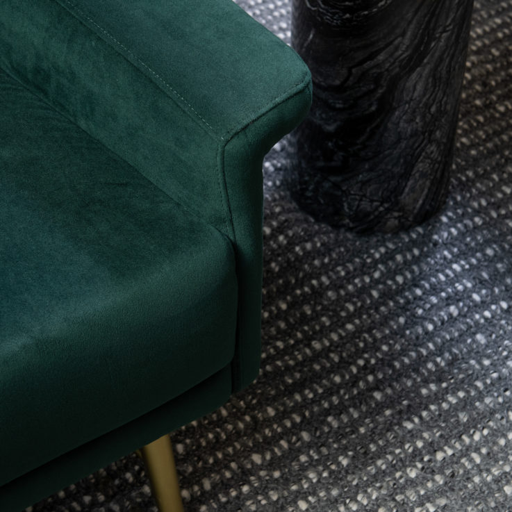 Closeup of the arm of a green chair and the golden endtable next to it