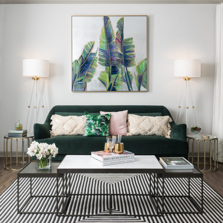 Green couch and coffee table beneath a large painting of leaves