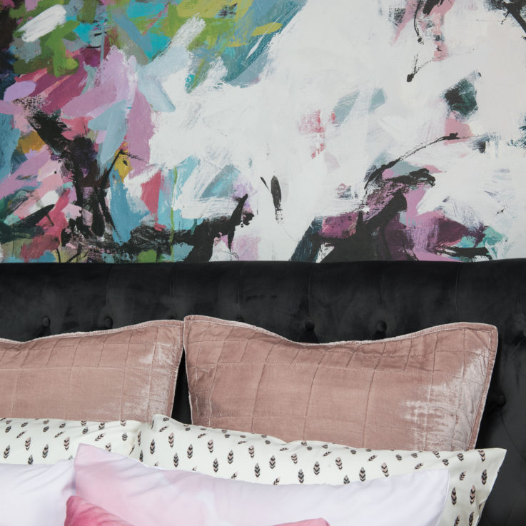 Closeup of a bed's headboard and pillows against an abstract painted wall