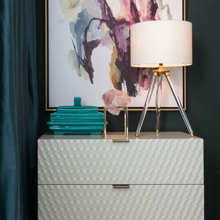 White nightstand with a lamp beneath an abstract painting