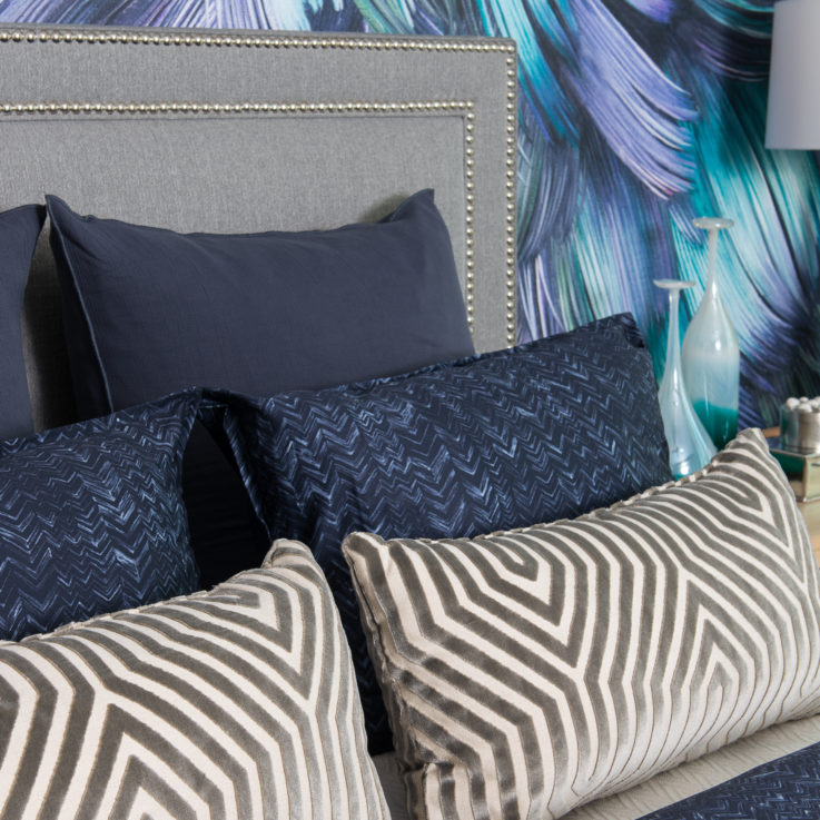 Blue, white, and gray pillows on a bed with a wooden nightstand